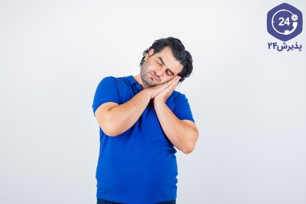 Mature man leaning on palms as pillow in blue t-shirt and looking sleepy , front view.